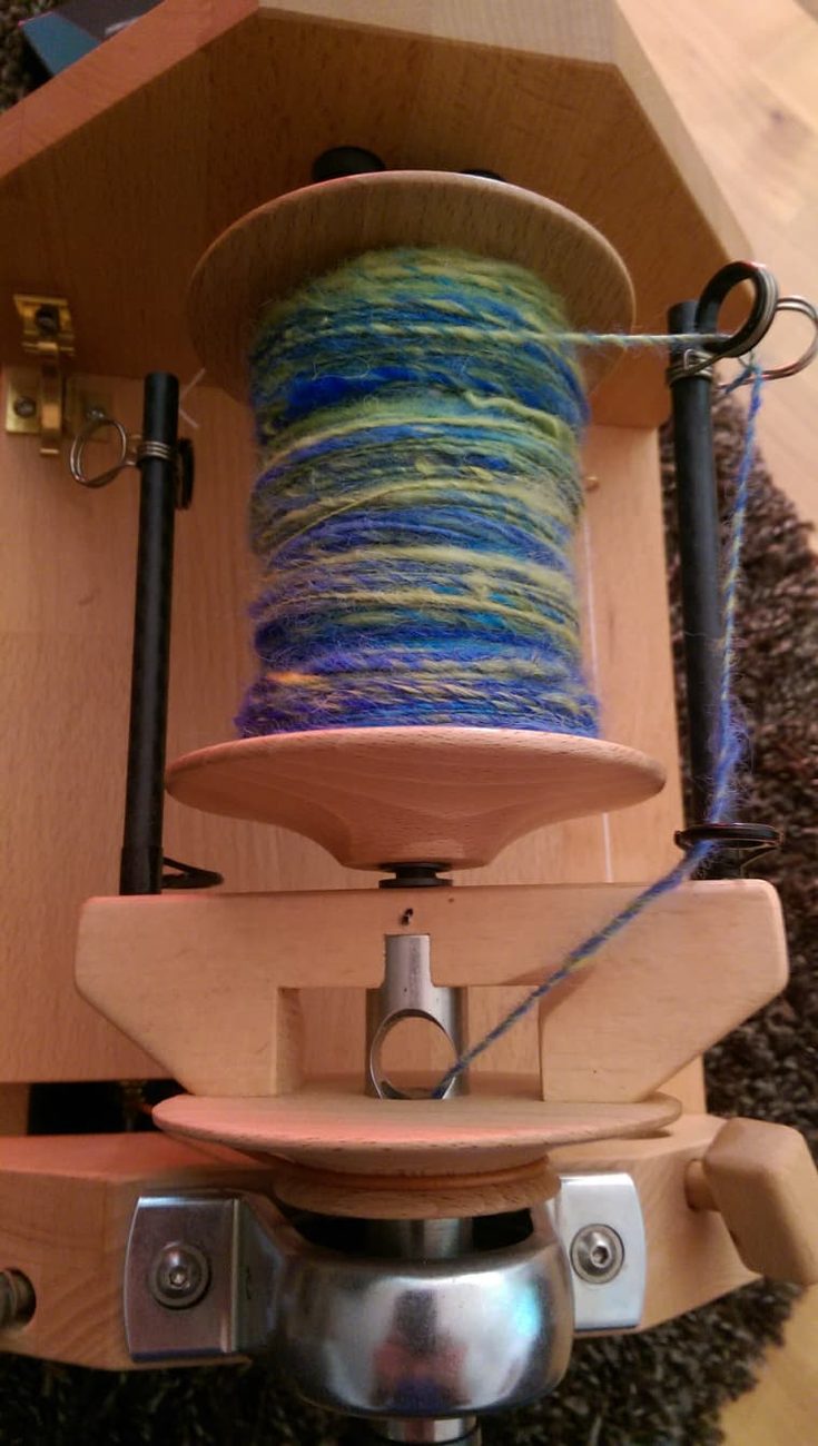 Spule des Zwirnzwerg mit aufgewickeltem blau-grünem Garn